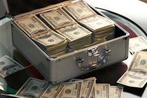 Open briefcase filled with stacks of hundred dollar bills on a glass table, representing wealth.